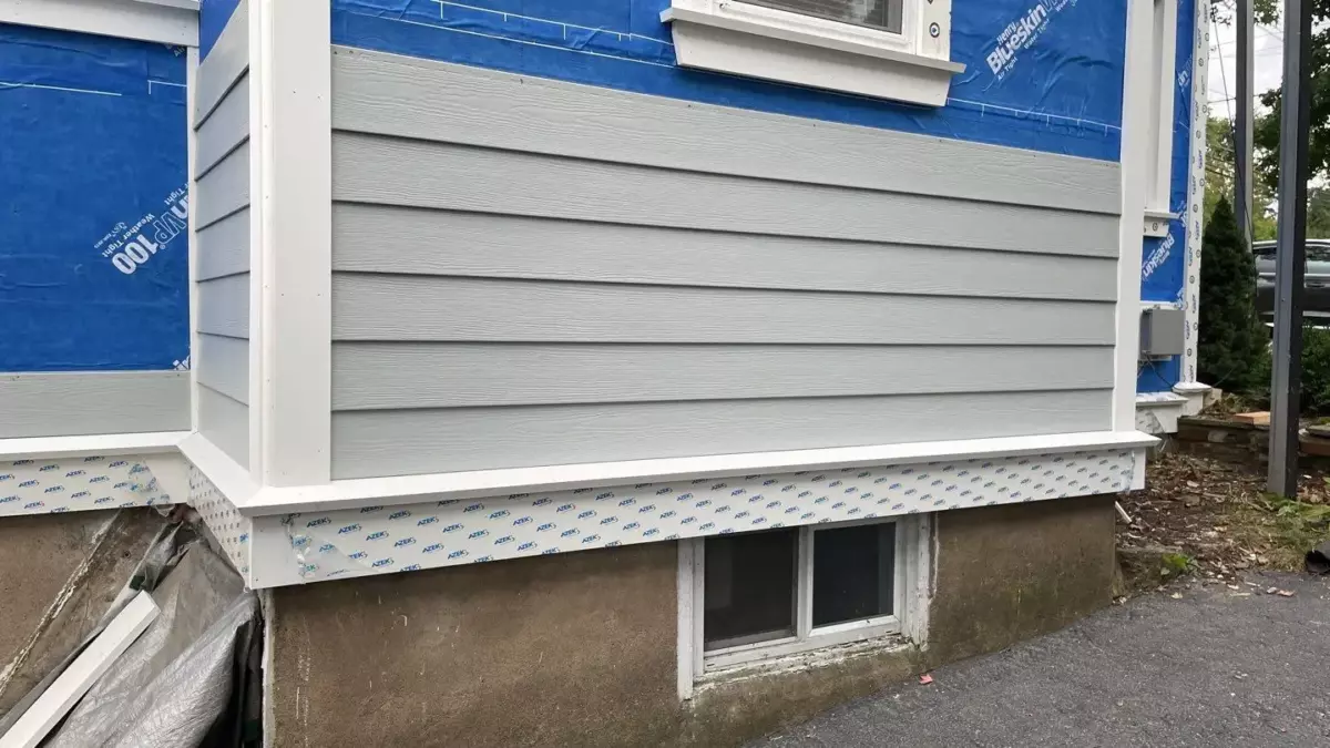 In-progress installation of gray fiber cement siding on a home, with visible blue house wrap and “Preferred Contractor” James Hardie badge.