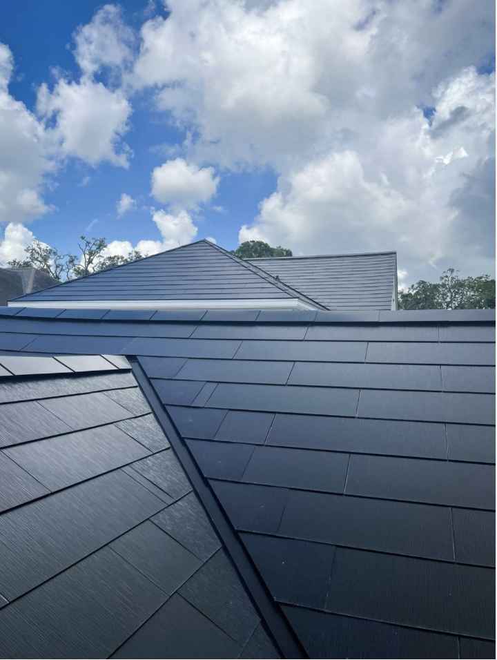Close-up view of a newly installed Tesla Solar Roof with sleek black solar shingles under a partly cloudy sky.