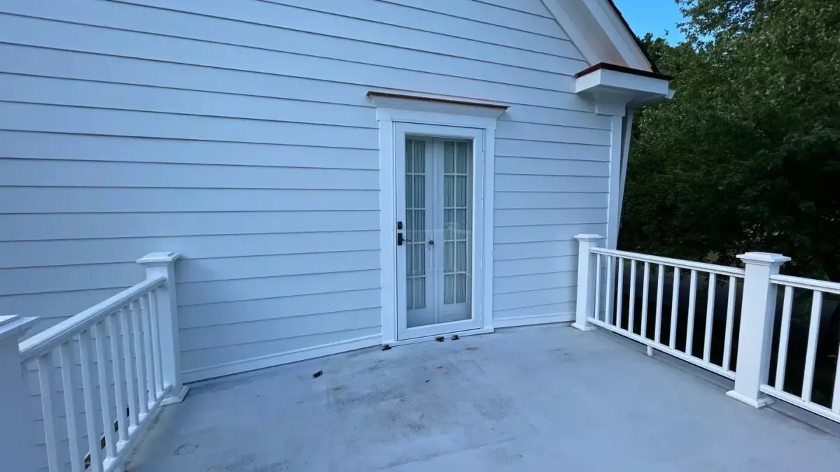 White vinyl siding on an exterior wall with a glass patio door and matching white railing surrounding a flat rooftop deck.