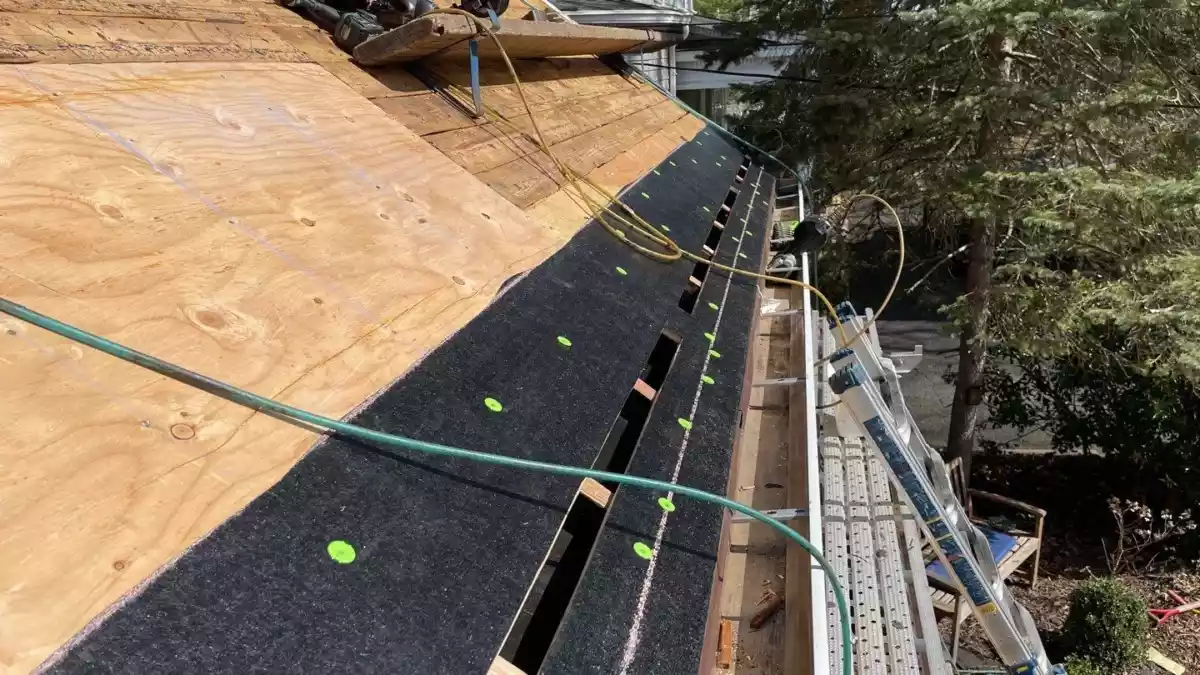 Roof decking with ventilation openings being prepped for intake air installation, showing black underlayment with green fasteners and exposed plywood.