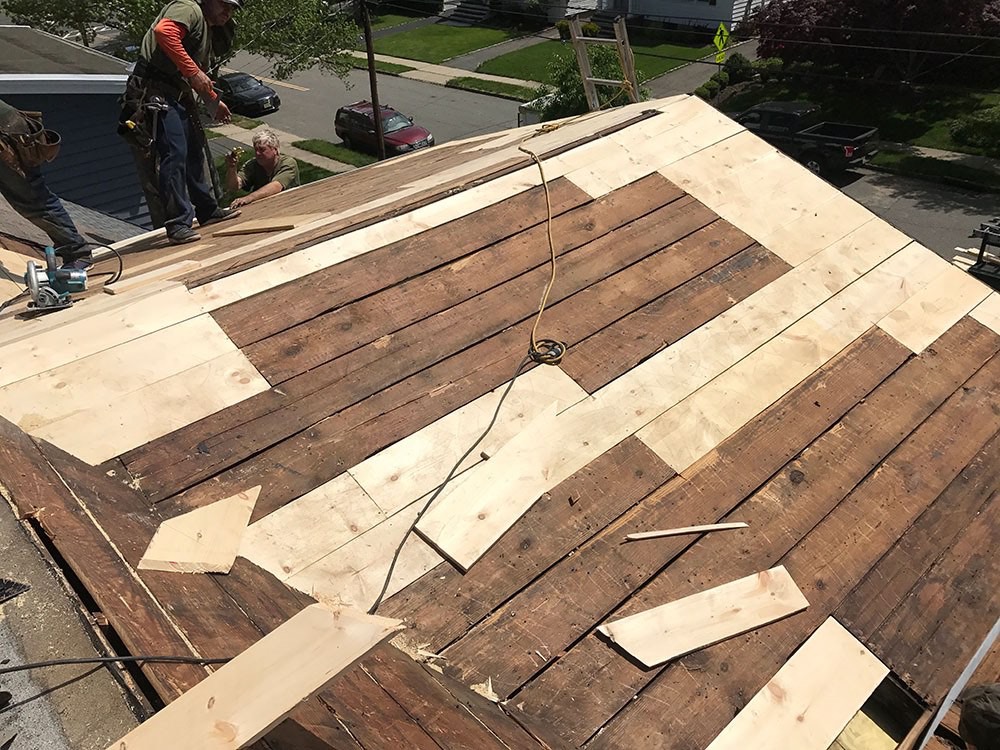 Roof deck repair in progress with mixed planks and plywood patches, showing roofing crew replacing damaged sub decking before installing new shingles.