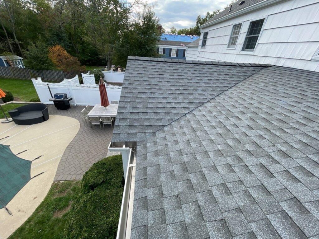 Toit en bardeaux gris récemment installé sur une maison blanche avec des gouttières propres, vue du dessus d'une cour avec mobilier de patio et piscine.