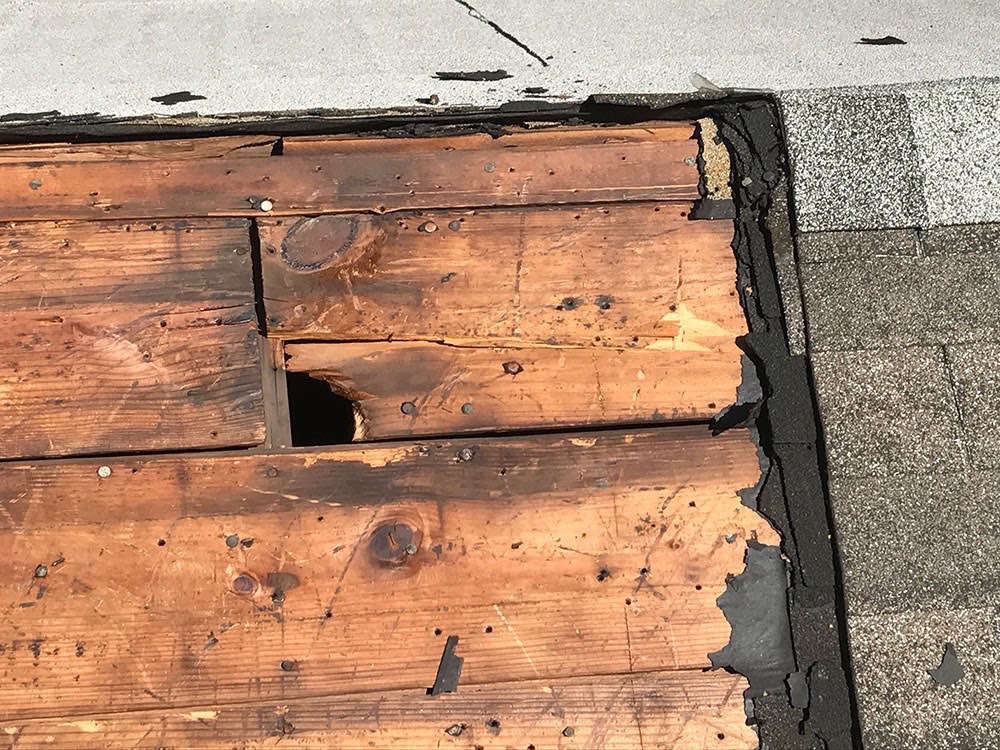 Exposed wooden roof decking showing signs of rot and damage during a roof tear-off, highlighting the repair process before new shingles are installed.