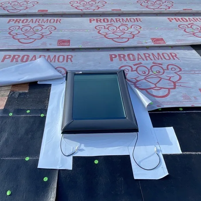A skylight installed on a roof during the repair process, surrounded by Owens Corning ProArmor synthetic underlayment and white flashing tape for waterproofing.
