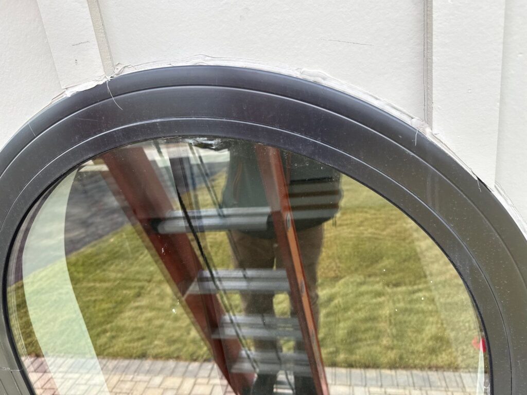 Close-up of radius window head showing failing caulk bead between window frame and siding with no underlying head flashing on new construction home