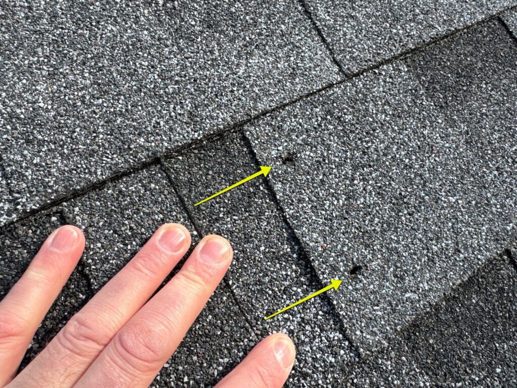Two unsealed through-the-deck holes in a new construction asphalt shingle roof left by pump jack scaffolding brackets after the siding crew removed the brackets