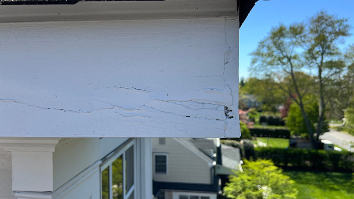 Dormer fascia board with surface cracking, paint delamination, and rot at corner intersections